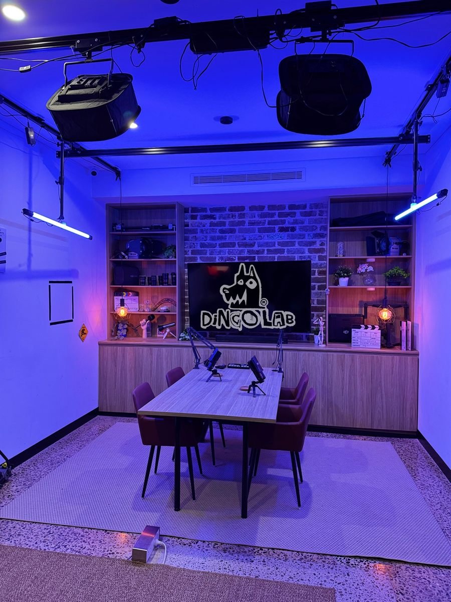 The Dingo Lab podcast set lit in blue, with a table for four and the studio logo on screen